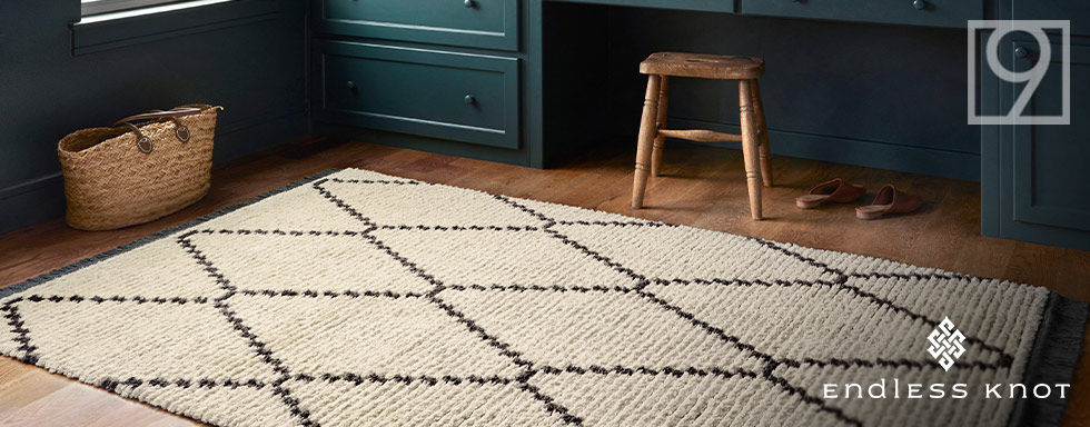 Tan woven rug on the floor with a black diamond outline pattern on it.